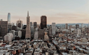 Aerial view of a cityscape with various skyscrapers and buildings under a cloudy sky, during what appears to be early morning or late afternoon.