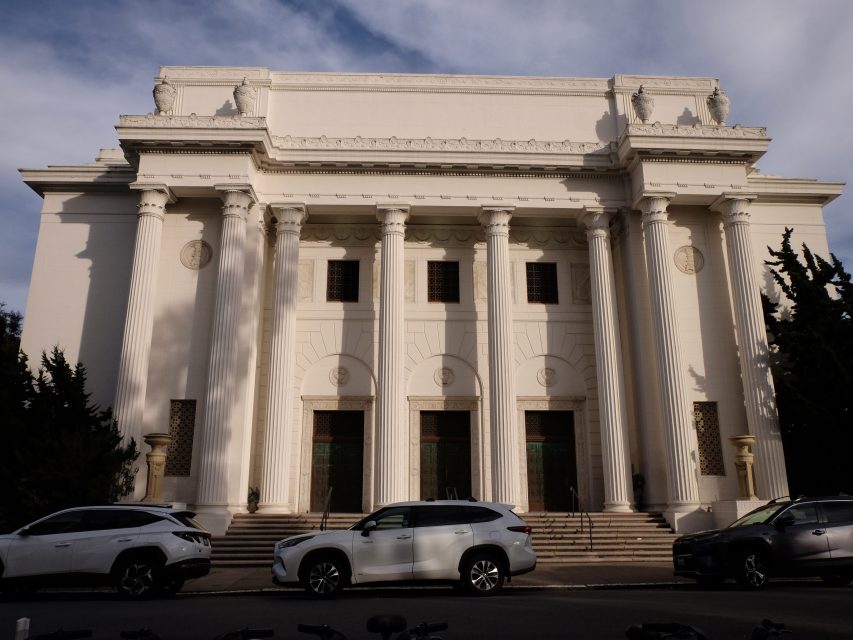 Exterior of a classical white building with tall columns and parked cars in front.