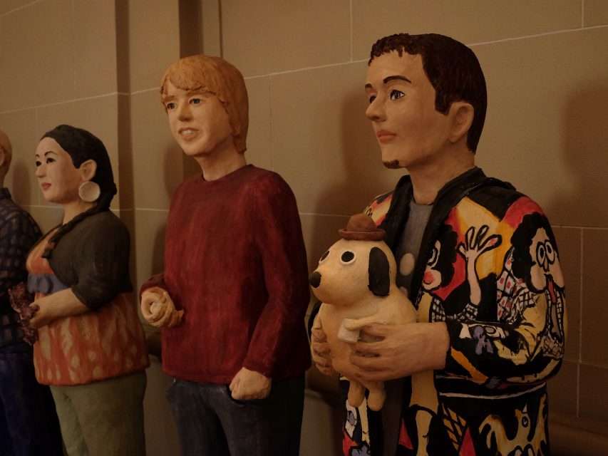 Four life-sized sculptures of people in colorful attire stand in a row, with one holding a dog figurine.