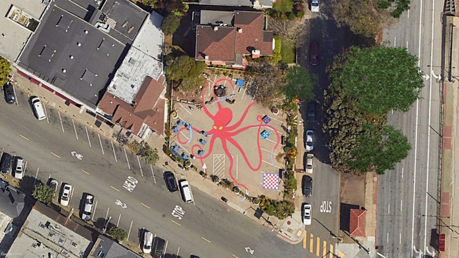 Aerial view of a playground featuring a large red octopus design, surrounded by roads and buildings.