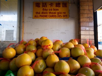 A stack of yellow grapefruits in red mesh bags is displayed under a sign advertising a phone cards discount in multiple languages.