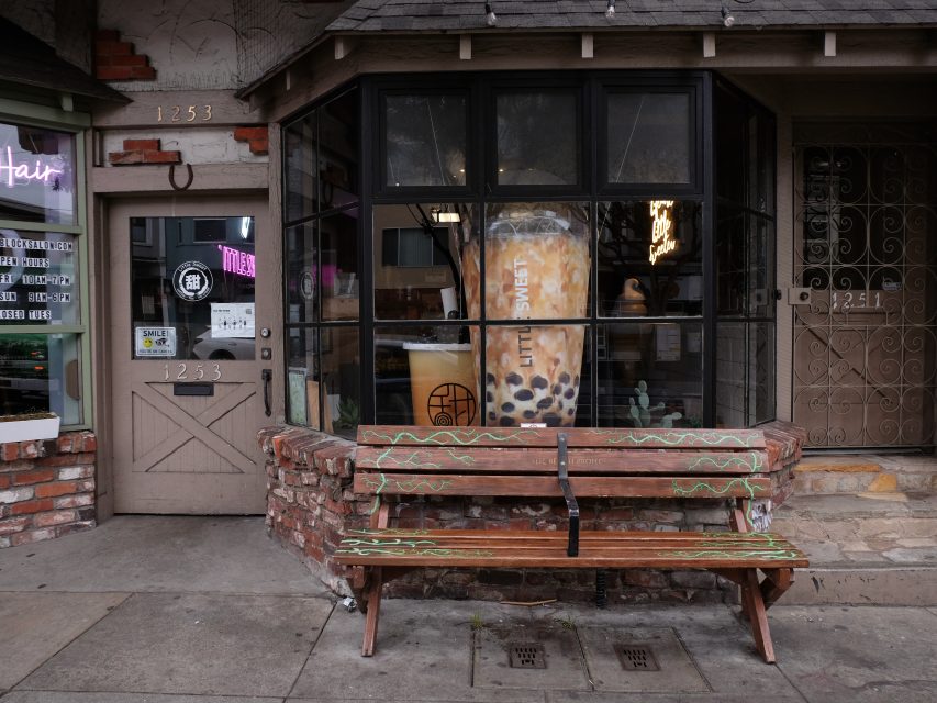 Storefront with a large boba tea poster in the window and a wooden bench outside. The door on the left has the street number 1235.