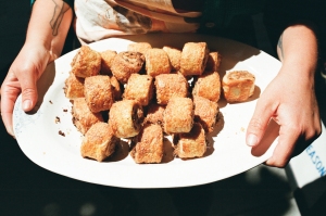A person holding a white plate filled with several crispy, golden-brown sausage rolls.