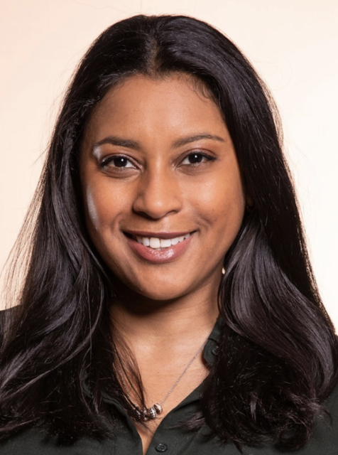 A person with long dark hair smiles at the camera against a neutral background.