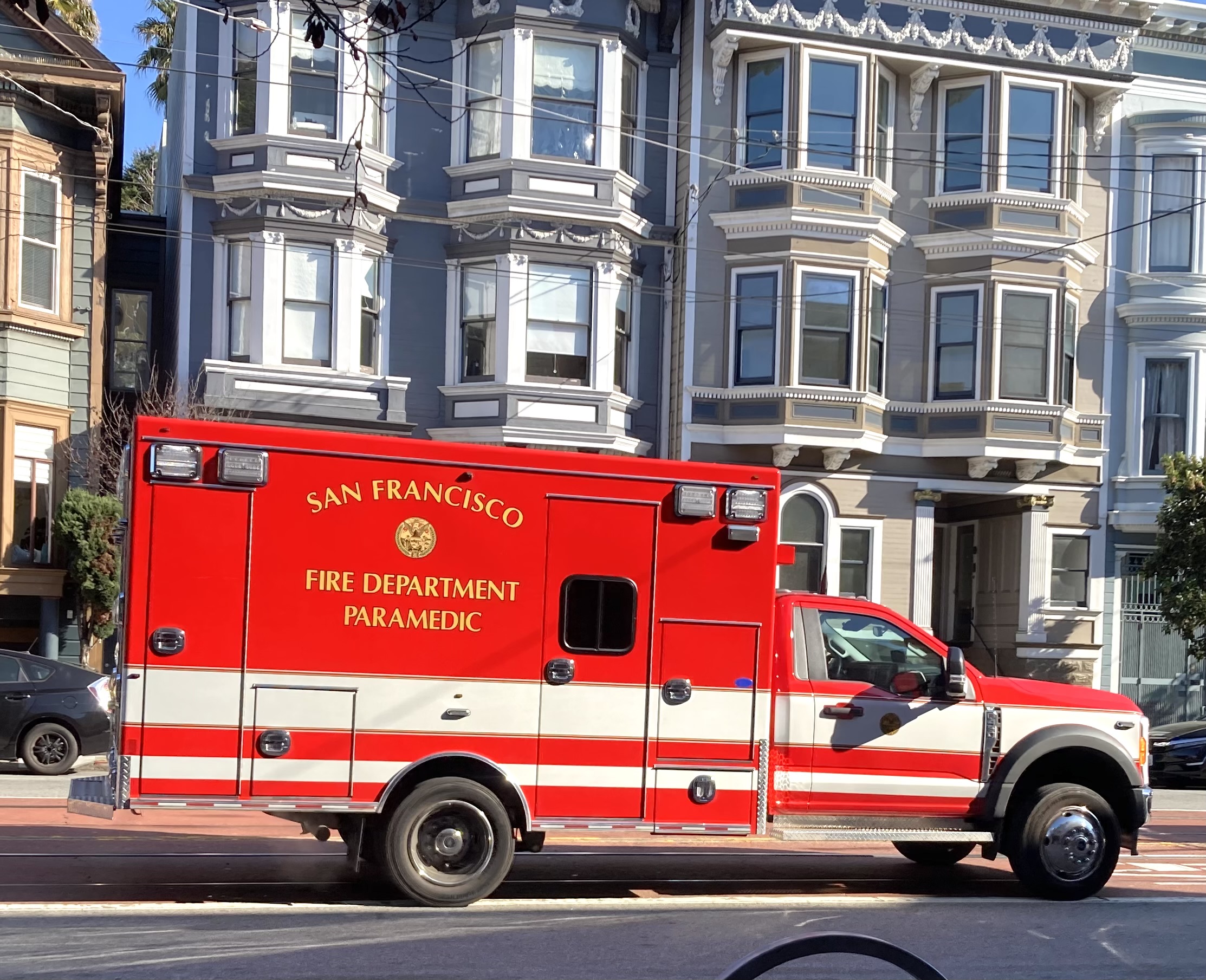 Red San Francisco Fire Department paramedic ambulance parked on a street with Victorian-style buildings in the background.