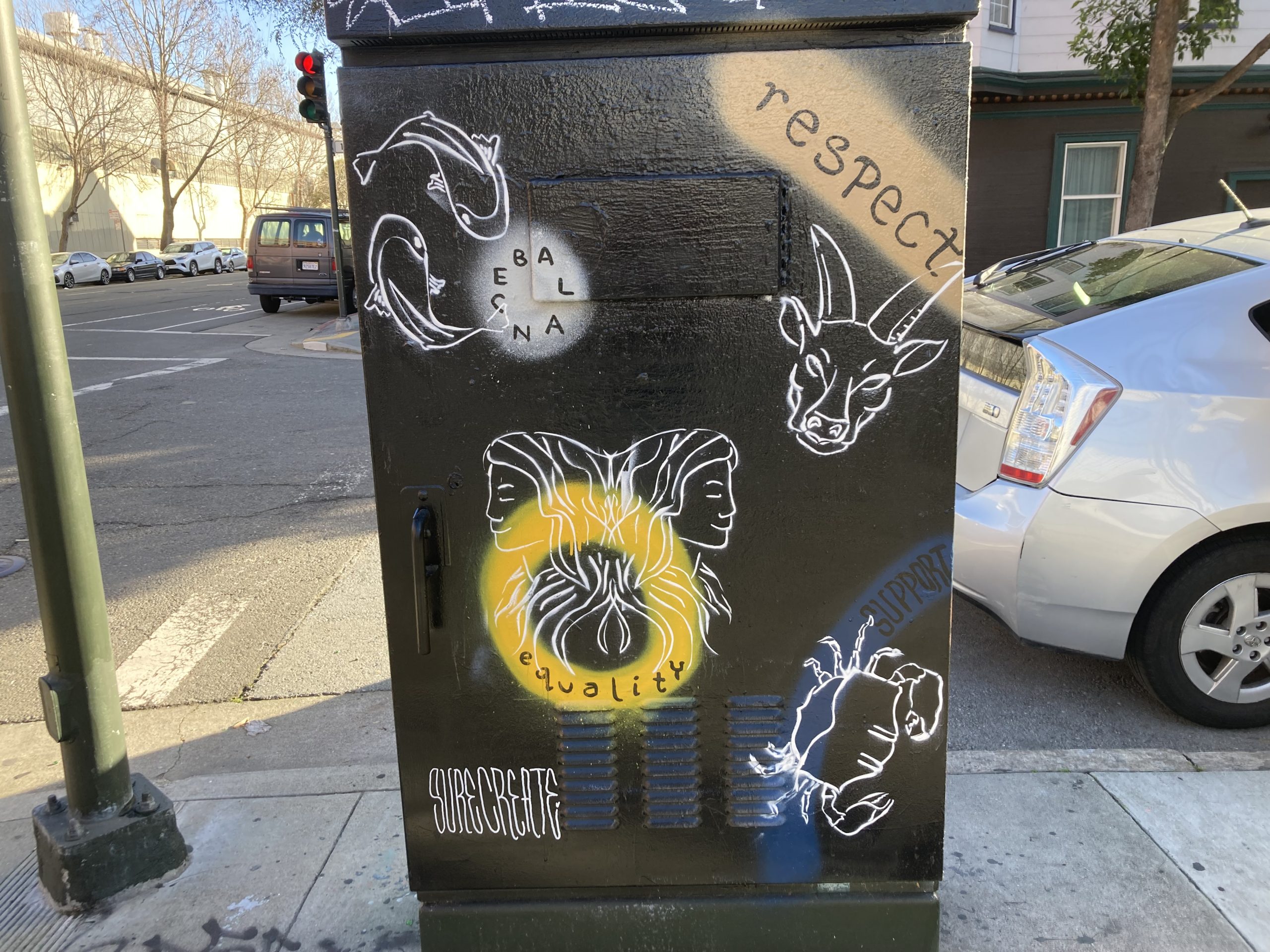 Utility box with street art featuring animals, abstract faces, and text like "respect" and "equality" at a street corner.