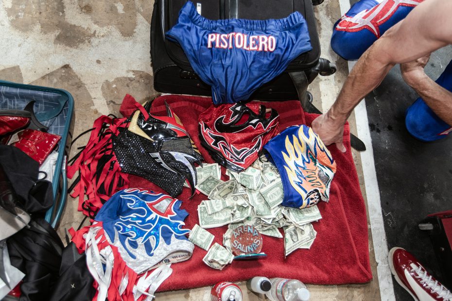 Luchador masks, costumes, and cash laid out on a red towel.