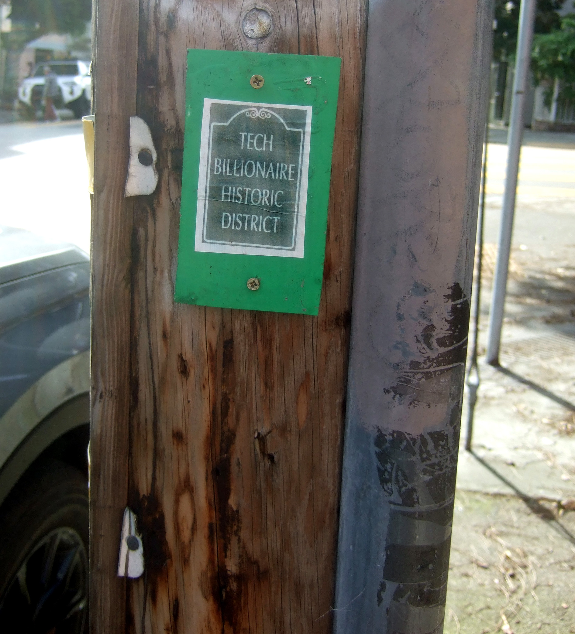 A small green and white sign on a wooden pole reads "Tech Billionaire Historic District."