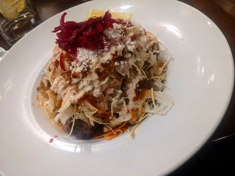 A dish served on a white plate featuring shredded vegetables, grated cheese, and red pickled topping, covered in creamy sauce.