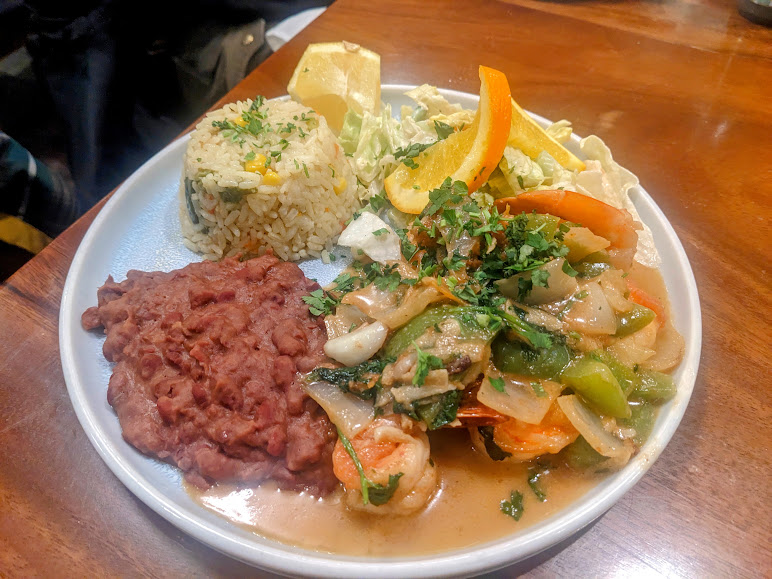 A plate of food with rice, refried beans, mixed vegetables, and shrimp in sauce, served with lettuce and a lemon wedge.