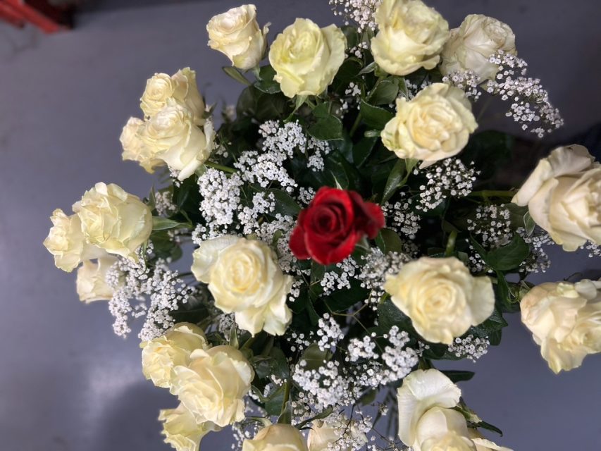 A bouquet of cream roses with one central red rose, surrounded by white baby's breath flowers, on a gray background.