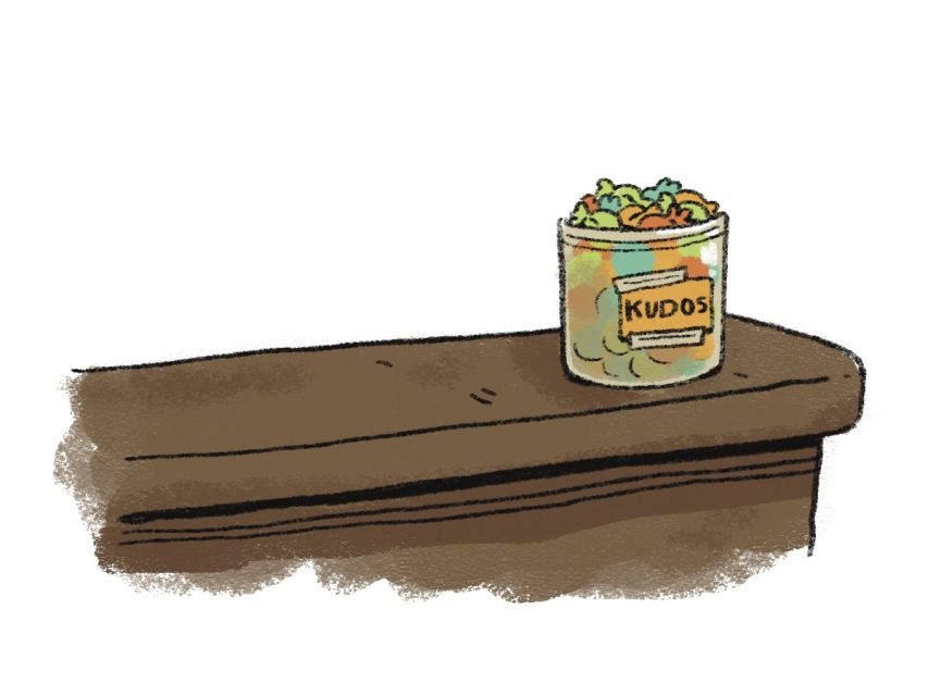 A glass jar labeled "Kudos," akin to a treasure in the candy court, brims with colorful sweets and rests elegantly on a wooden shelf.