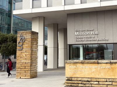 Entrance to Mission Hall, Global Health & Clinical Sciences Building, with a person walking nearby and visible UCSF signage.