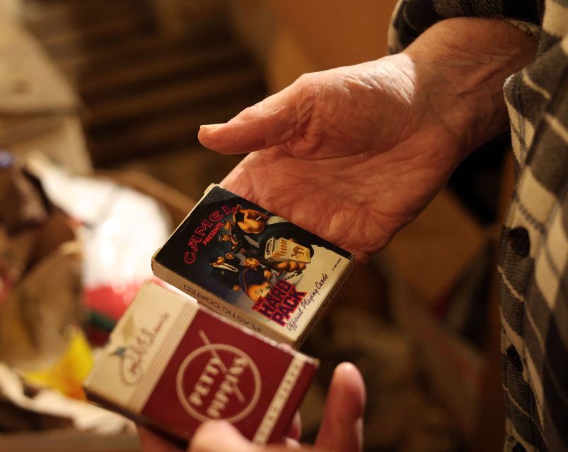 A person holding two sets of playing cards; one features a comedy theme "Cheech & Chong," and the other appears more traditional with partial red and white design visible.