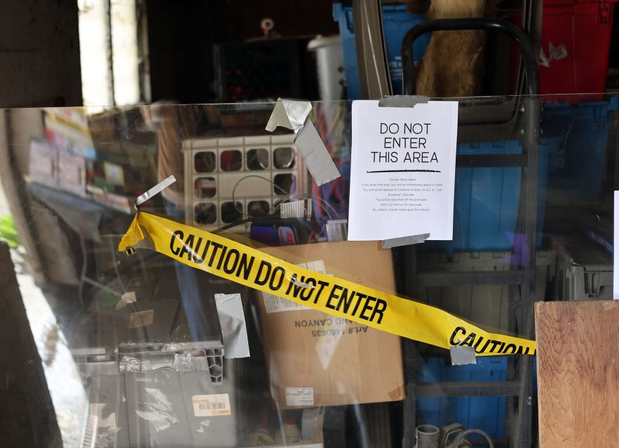 Cluttered area with "Do Not Enter" sign and yellow caution tape. Various items, including storage bins and boxes, visible behind the barrier.