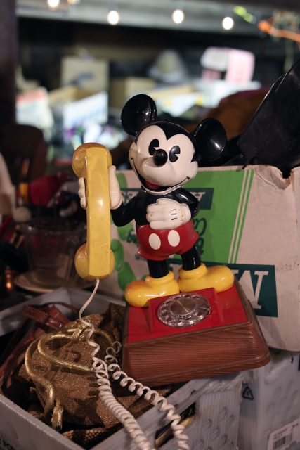 A vintage rotary phone featuring a character holding a yellow handset, surrounded by assorted items in a dimly lit setting.