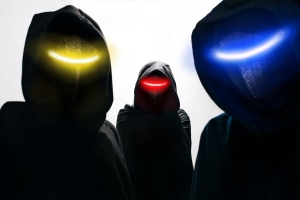 Three hooded figures with dark cloaks and glowing eyes—yellow, red, and blue—stand against a light background.