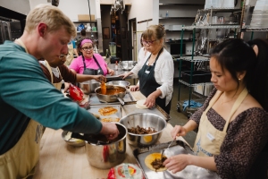 A group of people work together in a kitchen, preparing food with various bowls and ingredients on the counter.