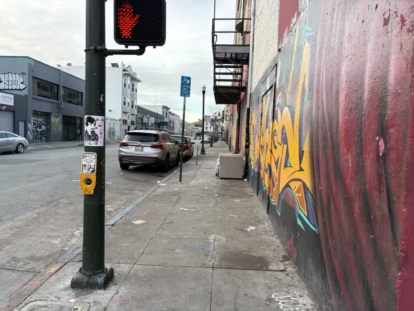 Urban street scene with graffiti on the wall, a crosswalk signal, a parked car, and buildings in the background.