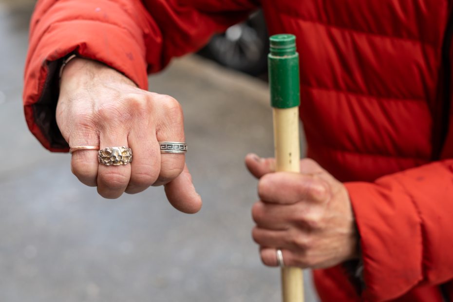 Person wearing a red puffer jacket holding a broomstick, showcasing rings on both hands.
