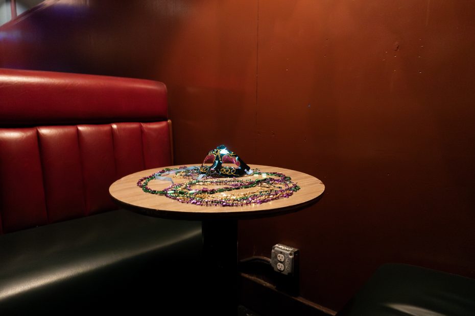 A table with colorful beads and a decorated mask on top, surrounded by red and black seating against a brown wall.