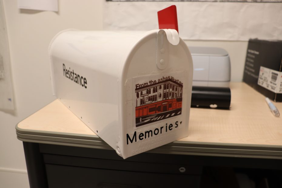 White mailbox with the word "Resistance" on the side and "Memories" on the front. A sticker with an image of the 22nd and Mission building is also on the front. A red flag is raised.