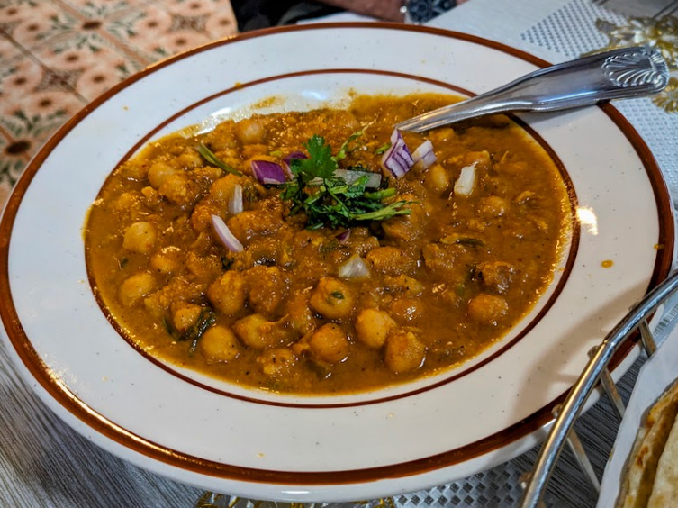 A bowl of chickpea curry garnished with cilantro and diced red onion. A spoon rests in the dish.