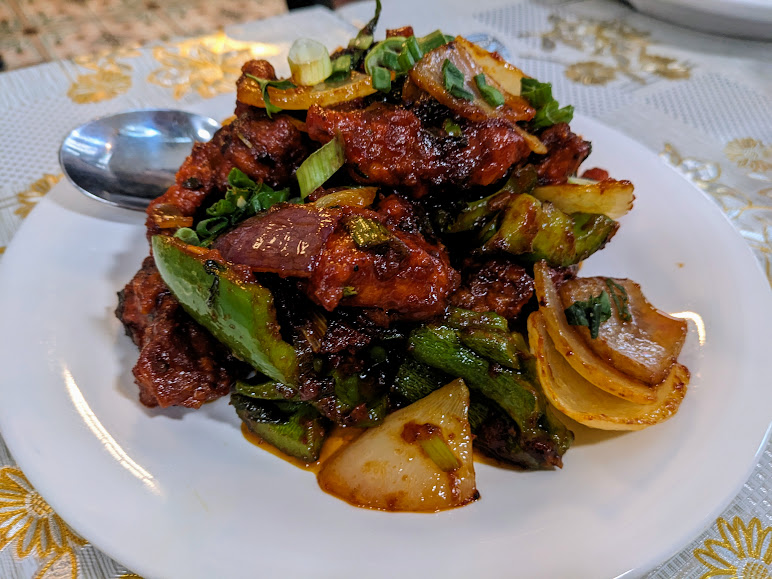 Plate of stir-fried beef with green peppers, onions, and green onions, served on a white plate with a spoon on the side.