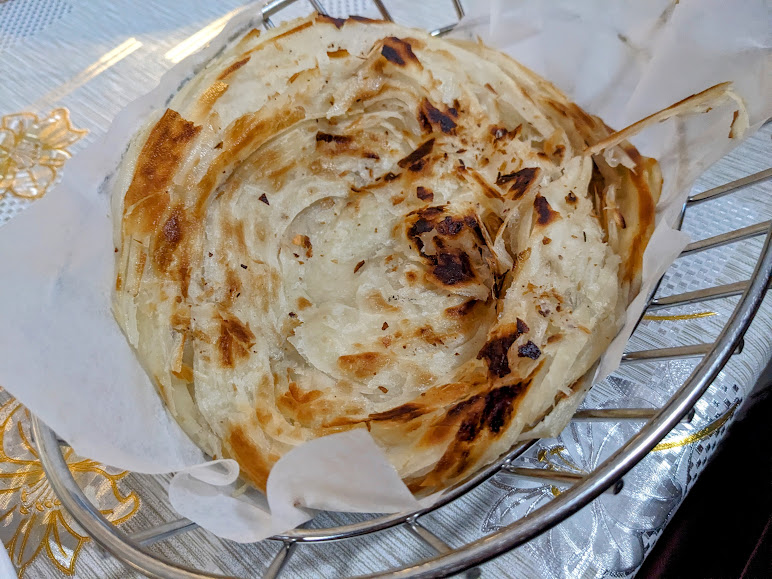 Close-up of a golden-brown, crispy flatbread served on white parchment paper in a wire basket.
