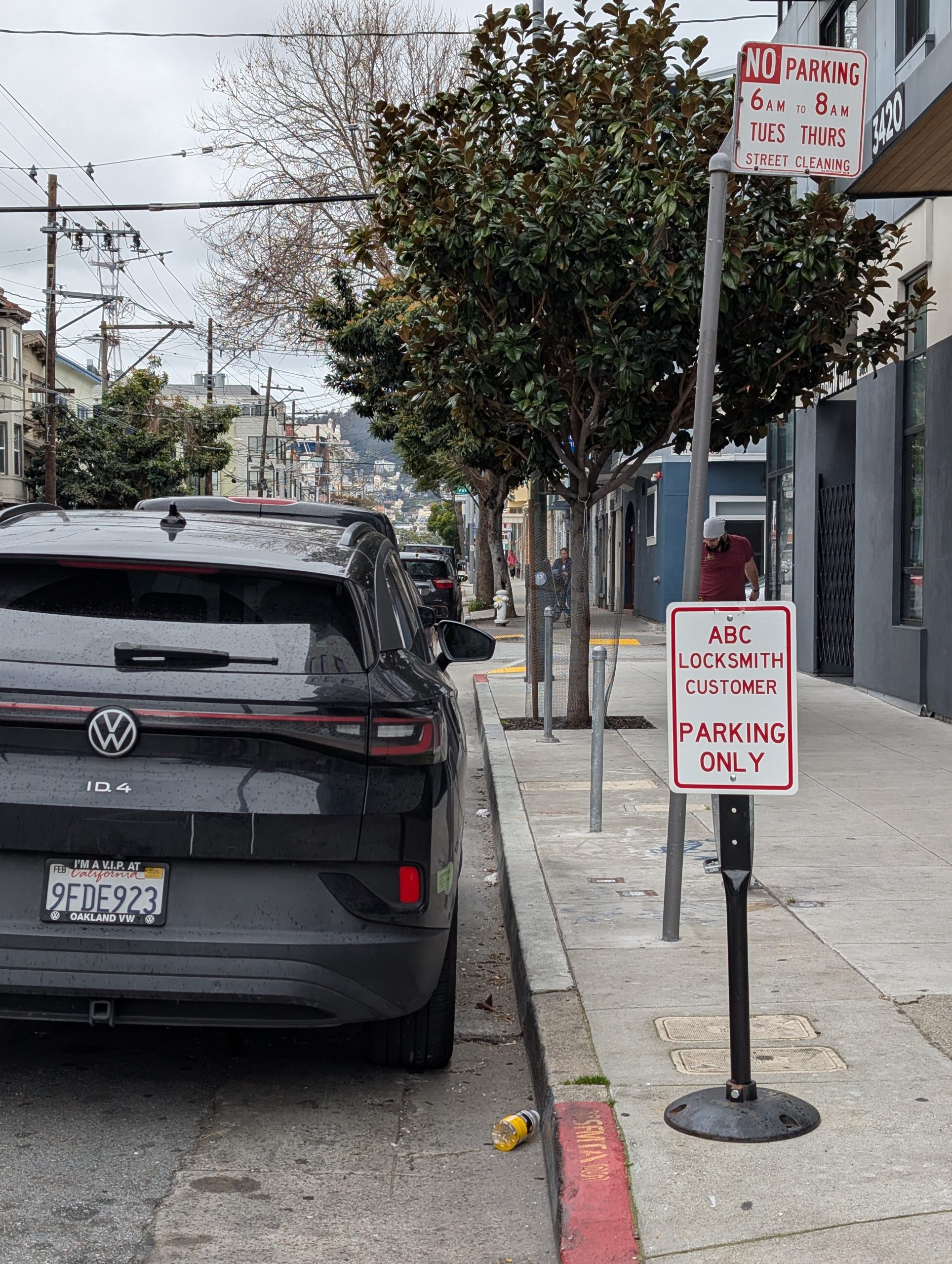 A black Volkswagen ID.4 is parked by the curb near a sign that says "ABC Locksmith Customer Parking Only" on a city street, with trees and a building in the background.