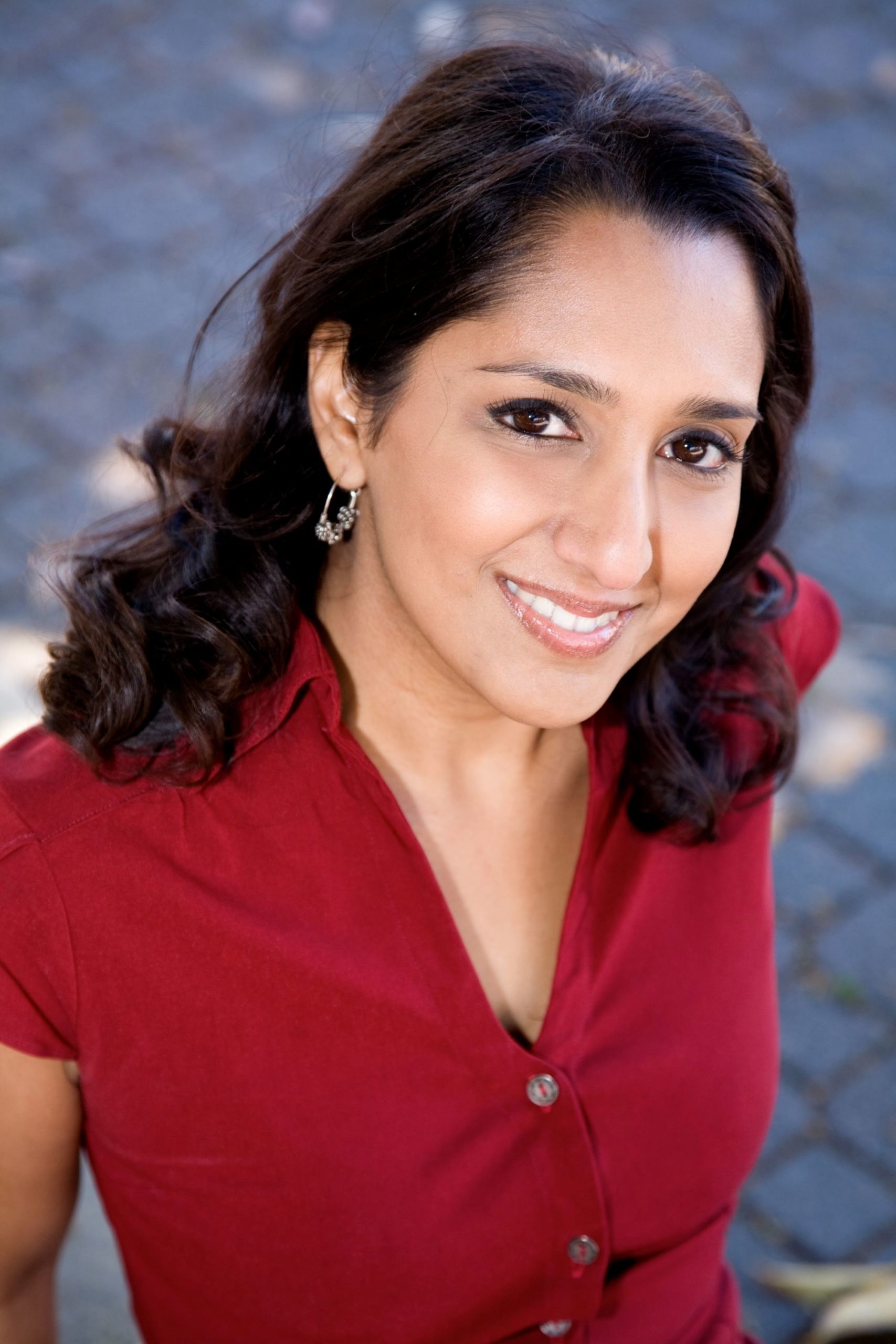 A person with dark hair, wearing a red shirt, smiles while looking upward. The background is a blurred, textured surface.