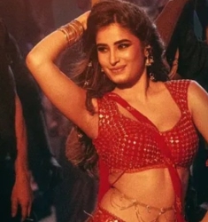 Person in red and gold dance attire poses with one arm raised, surrounded by others in a dimly lit setting.