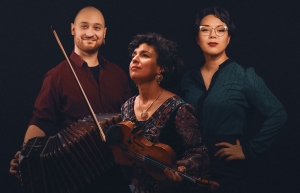Three individuals pose against a dark background. One holds a bandoneon, another has a violin. They each wear casual, colorful attire.