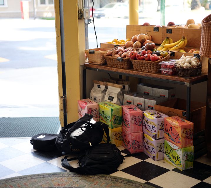 Grocery store entry with fruit baskets, boxes of LaCroix, and backpacks on the floor.