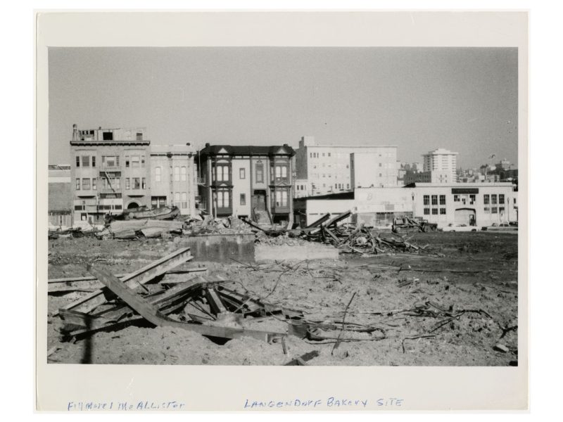 Demolished urban site with debris in the foreground, partially intact buildings mid-ground, and cityscape in the background.