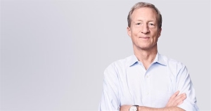 A middle-aged man with short gray hair stands with arms crossed, wearing a light blue shirt against a plain, light-colored background.