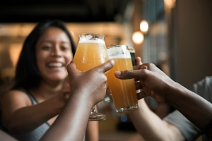 Three people toasting with glasses of beer, smiling in a casual setting.