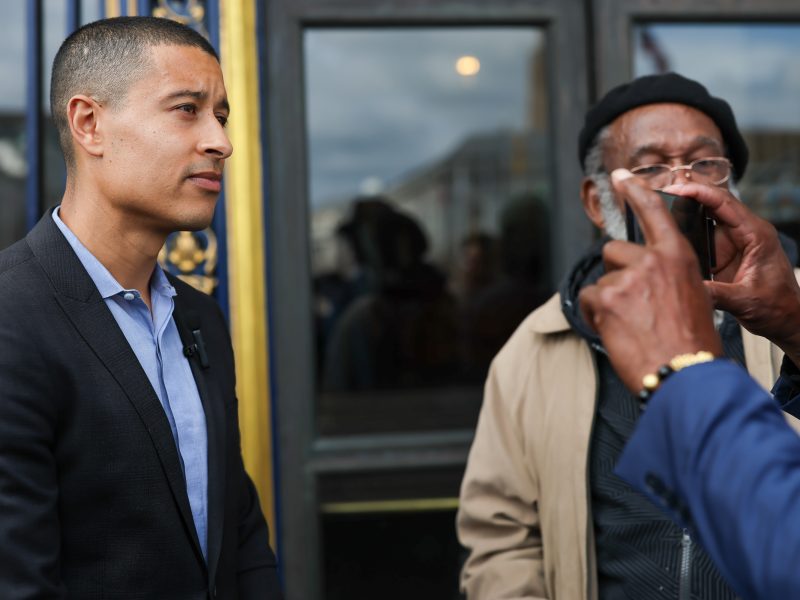 Two men stand outside a building with ornate details; one faces the camera while the other, channeling his inner Carter-Oberstone, captures the moment with a smartphone. Max Carter-Oberstone on the left.