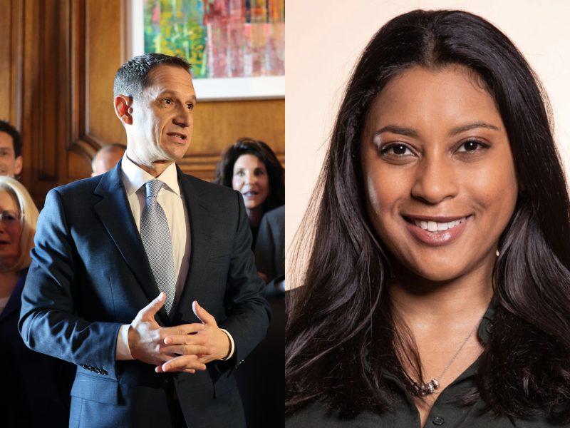 A man in a Lurie suit speaking with gesturing hands stands alongside a woman with long hair, smiling warmly at their engaging conversation.