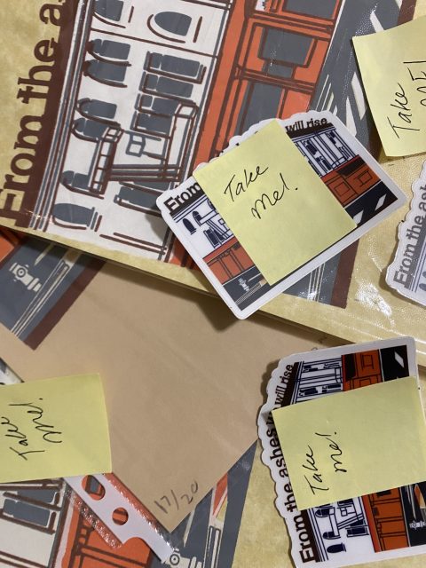 Assorted items with illustrated tram designs are scattered on a surface, featuring small cards and envelopes labeled "Take me!" on sticky notes.