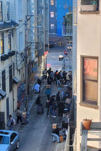 The bustling urban alleyway is alive with energy as people diligently sort and distribute boxes, surrounded by vibrant graffiti on the walls and a line of parked cars along the alleys.