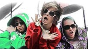 Three individuals wearing colorful hoodies and oversized sunglasses, posing with exaggerated expressions.