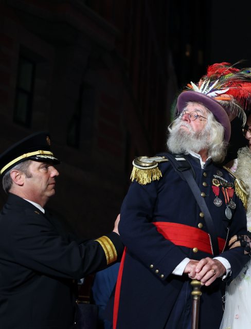 A man in a decorated military uniform with medals and a feathered hat stands beside another man in a dark uniform at night, possibly during events following the 1906 earthquake.