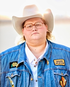 Person wearing a cowboy hat, glasses, and a denim jacket with patches, looking directly at the camera.