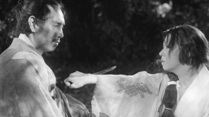 A person holds a knife to another person's chest in a tense moment, both wearing traditional Japanese clothing, in a black and white scene.