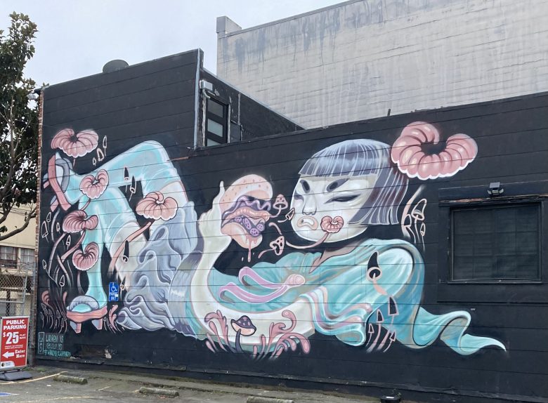 Mural on a dark building wall depicting a stylized figure with short hair, surrounded by large flowers, swirling teal shapes, and mushroom-like elements.