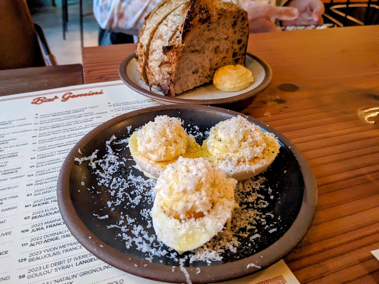 Three deviled eggs topped with grated cheese on a dark plate beside a menu and a smaller plate with slices of bread and butter.
