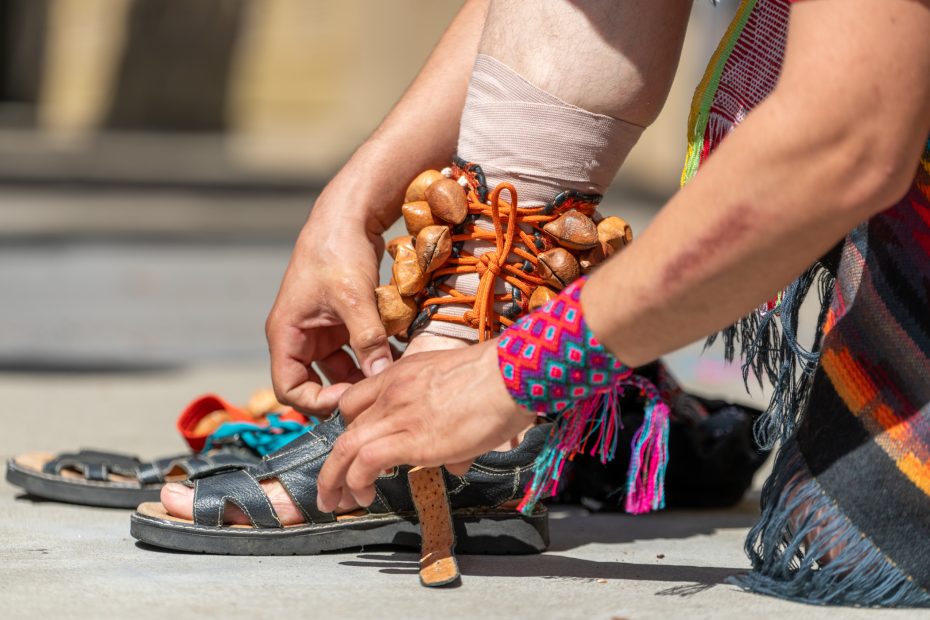 Person tying colorful sandals adorned with wooden beads and wearing a vibrant woven bracelet on the wrist.