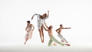 A group of four dancers perform on a white background, showcasing a mix of dynamic and poised movements.
