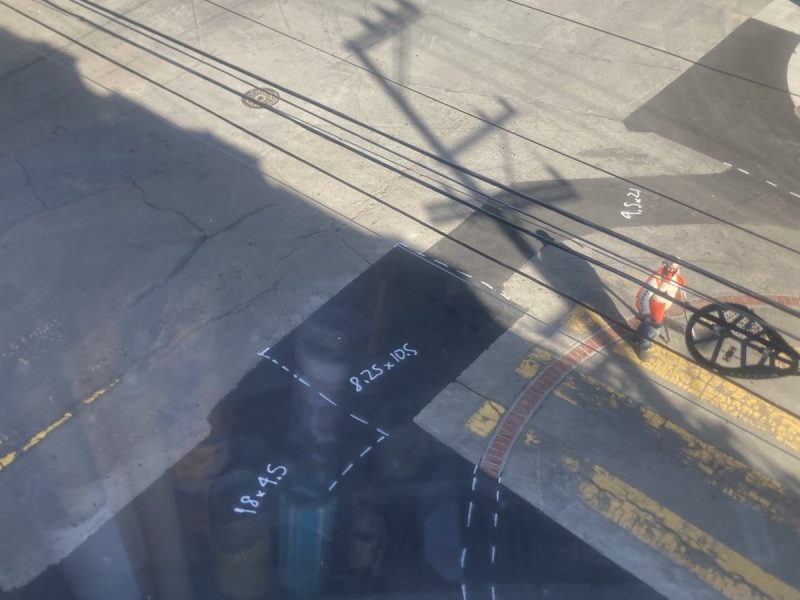 Aerial view of a street with visible power lines and shadows. Markings on the pavement indicate measurements, including "8.23 RG" and "18-45.